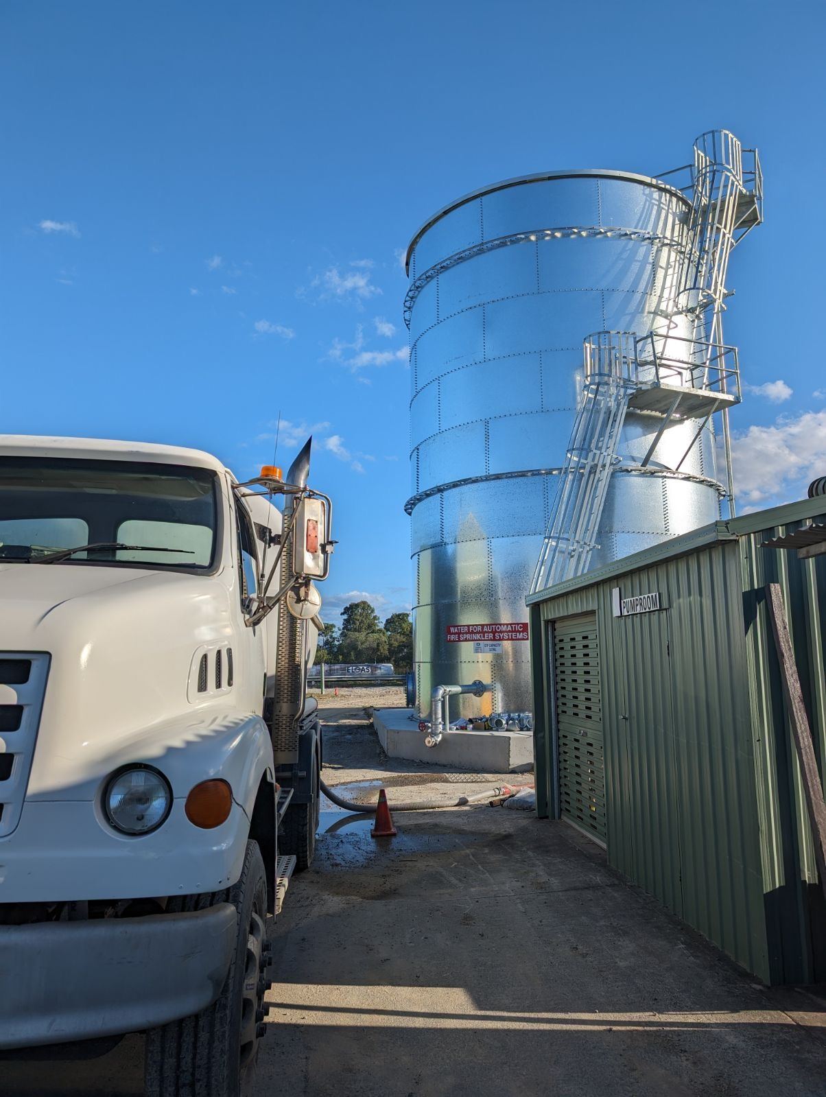 Water tanker filling a galvanised fire sprinkler system tank beside a pump room